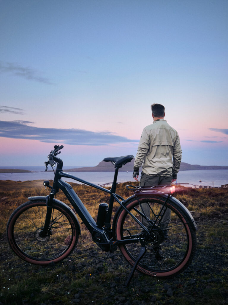Mann mit Kalkhoff Urban E-Bike genießt den Ausblick auf eine dämmrige Küstenlandschaft.